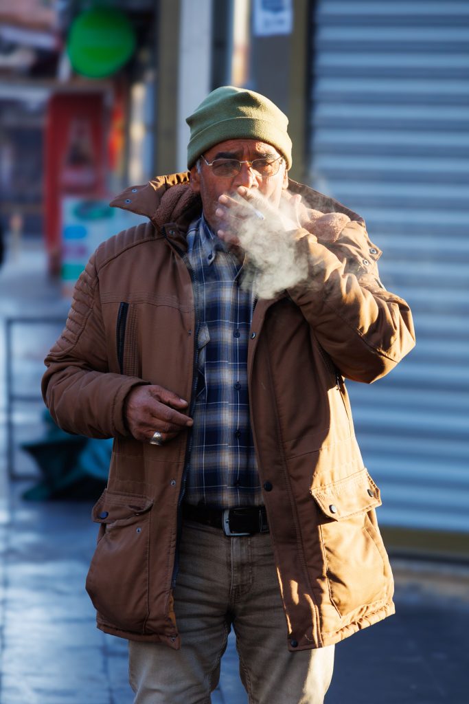 Elderly man smoking on a city street during winter afternoon.